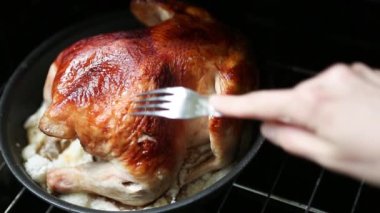 Aşçı çatalla pişmiş tavukla hazır olup olmadığını kontrol eder fırından fırın tutacağı ile altın bir kabuk çıkarır. Tuzlu tavuk, çatallı yumuşak kümes hayvanlarını delin.