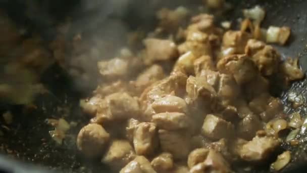 スロットスプーンで料理人の手は玉ねぎと肉の断片を攪拌している鋳鉄フライパンに油で揚げ 蒸気が来て 油が沸騰します 肉のシチュー 釜のバーベキュー クローズアップ — ストック動画