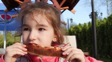 Kız komik ve açık hava parkındaki bir kafede iştahlı pizza yiyor. Sokak yemeği, aile zamanı, yürüyüş.