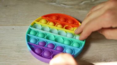 Çocuk stres önleyici silikon oyuncaklarla oynuyor. Parmaklar gökkuşağına, yumuşak kabarcıklara ve düğmelere basar. Çocuklar ve yetişkinlerde iyi motor becerilerin geliştirilmesi ve stres atımı için moda oyunu