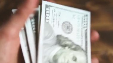 Elleri faturaları sayar, dolarları tahtadan bir masaya yatırır, banknotları çevirirler. Yüz dolar. Yakın plan 100 dolarlık banknotlar. Finans, ekonomi, mali planlama, ekonomi, tasarruflar.