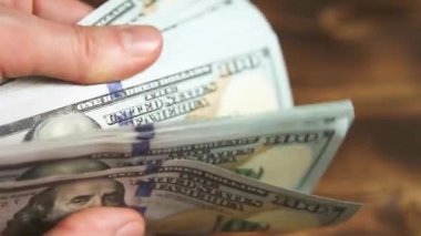 Elleri faturaları sayar, dolarları tahtadan bir masaya yatırır, banknotları çevirirler. Yüz dolar. Yakın plan 100 dolarlık banknotlar. Finans, ekonomi, mali planlama, ekonomi, tasarruflar.