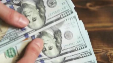 Elleri faturaları sayar, dolarları tahtadan bir masaya yatırır, banknotları çevirirler. Yüz dolar. Yakın plan 100 dolarlık banknotlar. Finans, ekonomi, mali planlama, ekonomi, tasarruflar.