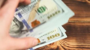 Elleri faturaları sayar, dolarları tahtadan bir masaya yatırır, banknotları çevirirler. Yüz dolar. Yakın plan 100 dolarlık banknotlar. Finans, ekonomi, mali planlama, ekonomi, tasarruflar.