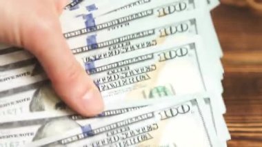 Elleri faturaları sayar, dolarları tahtadan bir masaya yatırır, banknotları çevirirler. Yüz dolar. Yakın plan 100 dolarlık banknotlar. Finans, ekonomi, mali planlama, ekonomi, tasarruflar.