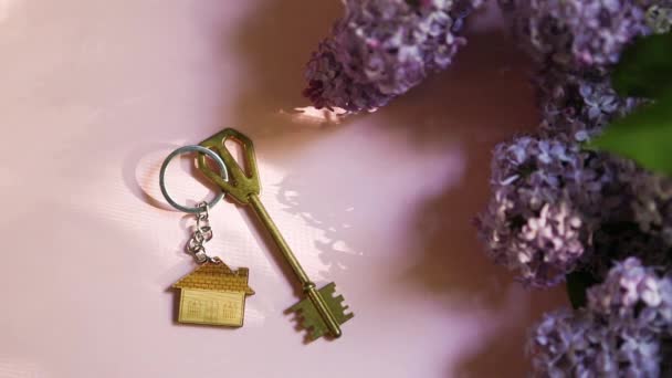 Hausschlüssel Mit Schlüsselanhänger Auf Rosa Federgrund Und Fliederfarbenen Zweigen Sommerferienhaus — Stockvideo