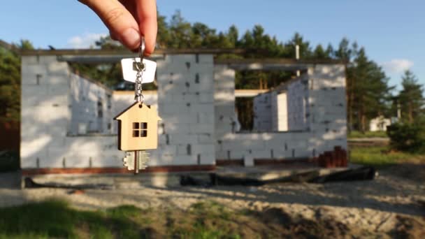 家の鍵リングとペンダントと建設現場 コテージの壁を背景に手の中でスイングキー 家を建て新しい家に引っ越し田舎の農場 — ストック動画