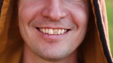 Kapüşonlu, gülümseyen beyaz adamın sarı dişleri. Dişlerine odaklan, ağzını aç. Diş problemleri, ölü dişler, diş beyazlatma, estetik restorasyon. Doğal diş minesi, vücut pozitif.