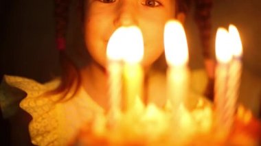 Kız pastadaki yanan mumlara bakar ve bir dilek diler. Doğum günü, mum ateşi, turuncu ateş, bir çocuğun mutlu gözleri. Çocuk tatili. Yakın plan.