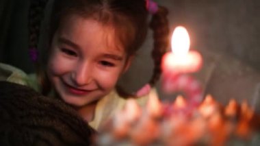 Kekin üzerinde 5 numaralı mumla yanan mumu seyreden kız, bir kedi tutarken dilek tutar ve komiktir. Doğum günü, beşinci yıl dönümü, beş yıl, mum ateşi, turuncu yangın. Çocuk tatili. Yakın plan.