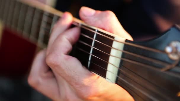 男はギターを弾き 日没時に屋外の歌を歌う ギターのフロントボードに手を置き 弦を通して指を動かし コードをクランプします インストゥルメンタル音楽 シート音楽のギターレッスン — ストック動画