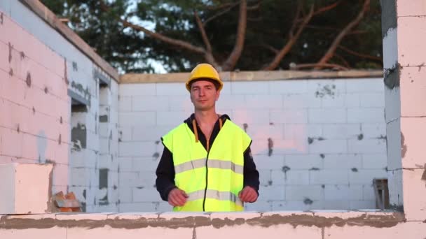 一名戴着黄色硬礼帽和反光背心的建筑工人站在建筑工地的窗台上 这所房子的墙壁是用砖 蜂窝混凝土砌成的 — 图库视频影像