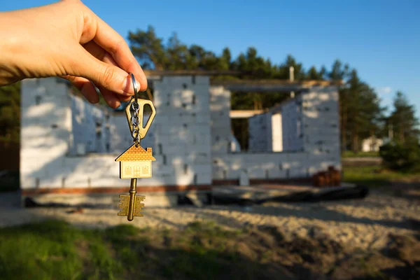 Hand with the key to the future house on the background of a construction site and walls made of porous concrete block. Building a home, moving to a new cottage, farm in the countryside