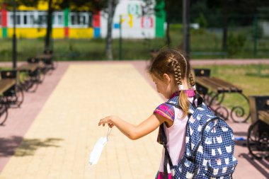 Dersten sonra okul yakınlarında sırt çantalı bir kız. Maskesi çıkarılmış, mutsuz, yorgun. Coronavirus enfeksiyonu, güvenlik önlemleri, önlem. 