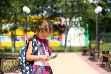 Okul bahçesinde okul üniforması içinde sırt çantalı küçük bir kız, pop it oyuncağı oynuyor. 1 Eylül 'de okula dönüyorum. Öğrenci dersten sonra dinlenir. İlköğretim, ilkokul öğrencisi