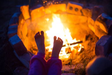 Ateşin altında çıplak ayaklar. Geceleri kamp ateşinin yanında, yazın açık havada, doğada buluşmalar. Aile kamp gezisi, kamp ateşi etrafında buluşmalar. Ayaklarını ısıt, soğuk gece