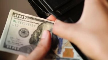 El siyah deri bir cüzdana 100 dolarlık banknot koyar ve bir banknot alır. Nakit para, 100 dolarlık banknotlar. Finans, ekonomi, mali planlama, ekonomi, tasarruflar.