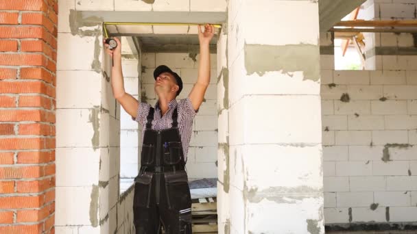 建筑工地的建筑工人用胶带测量窗户和砖墙的长度 小屋由多孔混凝土砌块 防护服和防弹衣组成 — 图库视频影像