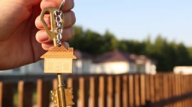 Anahtarlığı elinde anahtarlık olan anahtarlık. Çitlerin ve kulübenin arka planı. Yeni bir eve taşınmak, ipotek, emlak almak, konut kiralamak ve rezervasyon, köyde yaşama hayali. Boşluğu kopyala
