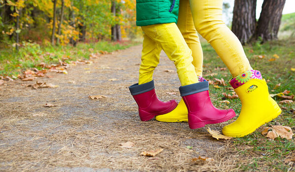 Ноги в красных и желтых резиновых сапогах матери и дочери в осеннем лесу. Сезональность, сезоны, опавшие сухие кленовые листья, семейная прогулка, чувство любви и заботы, родительство