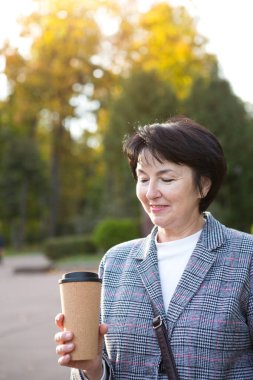 Parktaki hanımefendinin portresi ve yanında tekrar kullanılabilir plastik bir fincan kahve. Geri dönüşüm ve ekoloji, sıfır atık. Temiz havada bir yürüyüş, 50 yıl mutlu bir çağ.