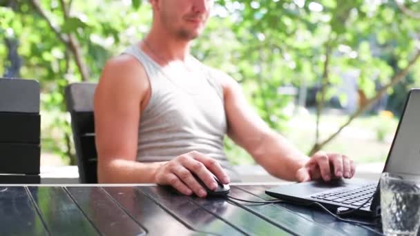 在室外庭院里的笔记本电脑前工作 一个穿着T恤衫的男人正坐在桌旁的一张野营椅上 家庭办公室 远程工作 远程位置 使用键盘和鼠标 — 图库视频影像