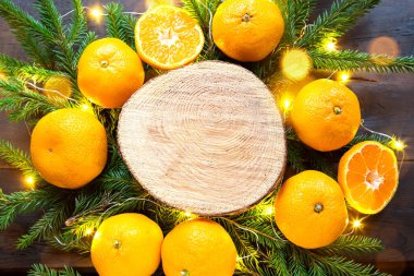 Mandalinalar, köknar dalları ve altın ışıklı çelenklerle çevrili ağaç kesimindeki yeni yıl arkaplanı, yazı için ahşap alan. Citrus aroması, portakal dilimleri, Noel. kare