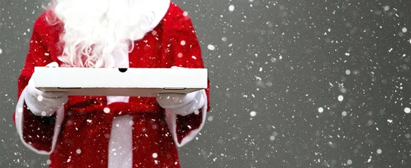 Beyaz eldivenli, sakallı, kırmızı ceketli Noel Baba 'nın ellerinde beyaz pizza kutusu. Noel fast food teslimatı. Yılbaşı arifesi terfisi. Bayramlarda yemek şirketinde çalışıyorum. Uzayı kopyala, taklit et. Pankart