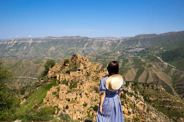 Dağıstan 'ın yüksek dağlarındaki kadın turist doğanın nefes kesen panoramik manzarasına ve terk edilmiş antik Gamsutl şehrine hayran. Kafkasya dağları, turistik yerler, harabeler, gezi turları.