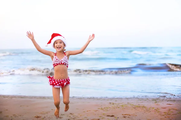 Kırmızı Mayo Kumsalda Noel Baba Şapkası Takan Yaşındaki Kız Mutlu — Stok fotoğraf