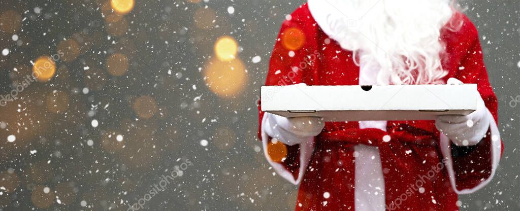 White pizza box in the hands of Santa Claus in white mittens, with a beard, in a red coat. Christmas fast food delivery. New year's eve promotion. Work on public holidays catering. Copy space, mock up. Banner