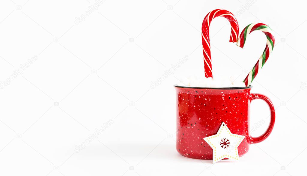 Red mug with marshmallows and caramel candy cane in the shape of a heart on a white background and a Christmas tree toy a wooden star. Christmas, New Year, festive mood. Copy space