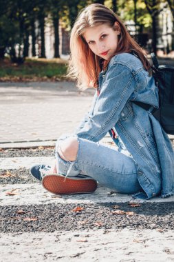 Sıradan bir sokak tarzında oturan kot elbiseli bir kız. Açık havada güneşlenen bir genç.