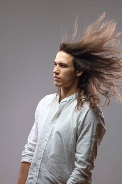 Uzun saçlı yakışıklı adam. Hareket halindeki yakışıklı adamın portresi. Stüdyoda beyaz gömlekli yalnız seksi bir çocuk var.