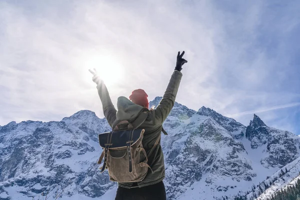 Happy person enjoy life with hands up on background of snow-capped mountains and blue sky with sun. Girl travels with backpack. Concept of freedom, journey, active lifestyle. Human and nature