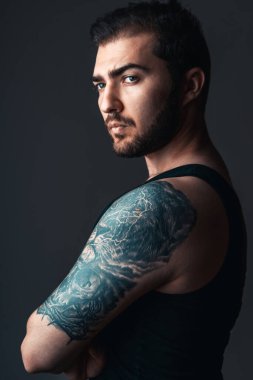 Stüdyodaki esmer yakışıklı adamın portresi. Kolunda siyah arka planda aslan dövmesi olan adam.