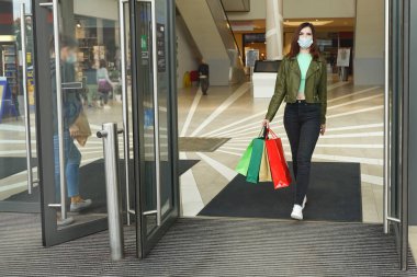 Alışveriş çantalı mutlu kadın alışveriş merkezinden çıkıyor. Koruyucu maskeli kız