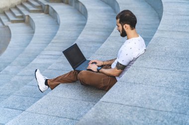 Dizüstü bilgisayarlı serbest çalışan adam basamaklar üzerinde çalışıyor. Uzaktan kumandalı işçi bilgisayarda yazıyor. Meşgul