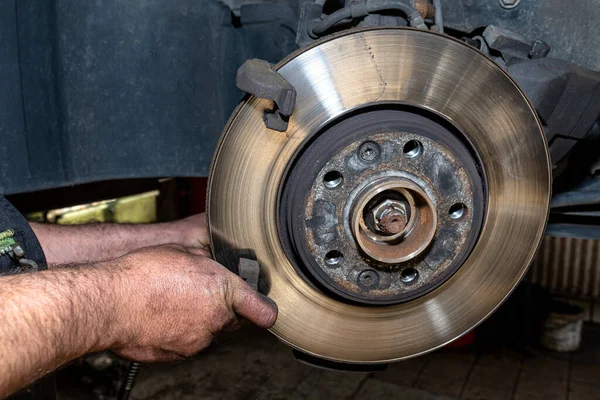 A car mechanic pulls a brake caliper in a car standing on a car jack in the workshop.