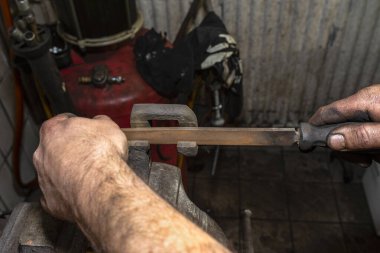 Tamirci, bankın mengenesine bağlı paslı fren kalibresini temizlemek için metal bir dosya kullanıyor..