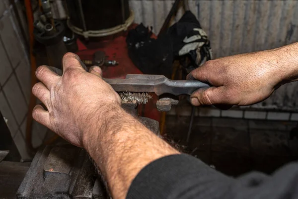 A mechanic cleans a rust-covered brake caliper attached to a bench vise with a wire brush.