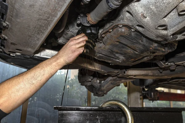 The car mechanic unscrews the diesel oil filter next to the oil pan, old black oil drains into the container.