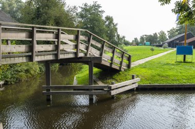 Hollanda 'da bitki ve binaların arka planındaki bir kanalın üzerindeki tahta süslemeli köprü..