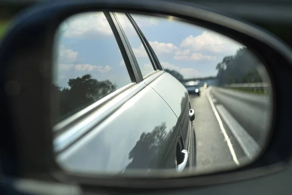 Reflection in the side mirror of a car driving on the highway, visible car in the reflection.