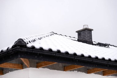 Ayrılmış bir evin çatısı bulutlu bir gökyüzüne karşı karla kaplıdır. Görünen sistem bacası fayanslarla ve düşen karla kaplı..