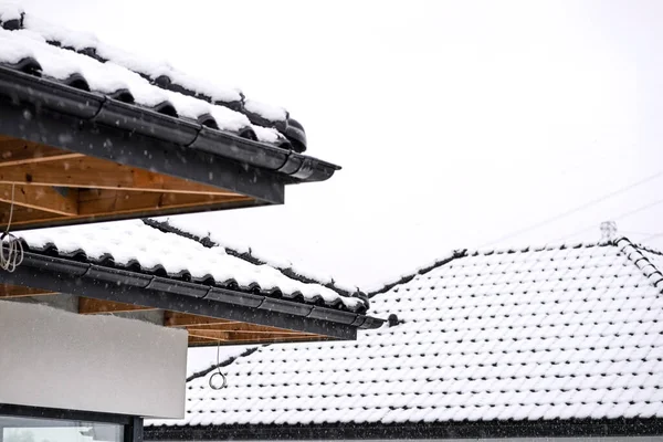 The corner of the roof of a single-family house is covered with snow against the cloudy sky, the ridge, roof trusses and falling snow are visible.