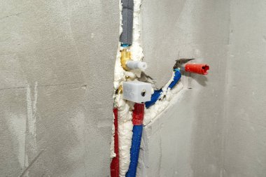 Gizli bir duşta alçıya yerleştirilmiş pirinç bir musluk. Yalıtılmış su boruları görünür..