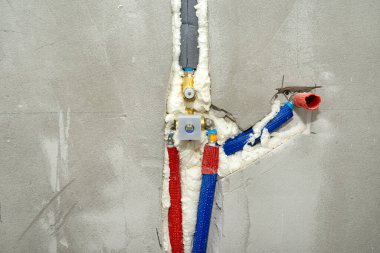 Gizli bir duşta alçıya yerleştirilmiş pirinç bir musluk. Yalıtılmış su boruları görünür..