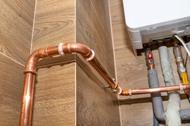 Doğal gaz tesisatı için bakır borular, seramik fayanslarla kaplı bir kazan dairesinin duvarına bağlı..