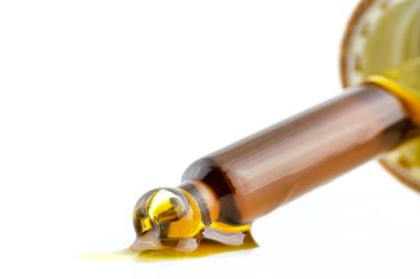 Cam bir pipetin makro görüntüsü ve beyaz üzerinde izole edilmiş kenevir özünden bir damla CBD yağı..